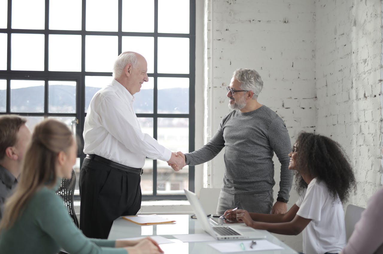 Group of diverse coworkers in office man middle aged and man senior shacking hands while working on project with colleagues